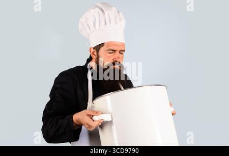 Cuoco maschile o cuoco in uniforme tenendo una grande pentola o una pentola e un pasto profumato. Gusta un delizioso odore di cibo. Il cuoco in grembiule tiene in mano la casseruola o grande Foto Stock
