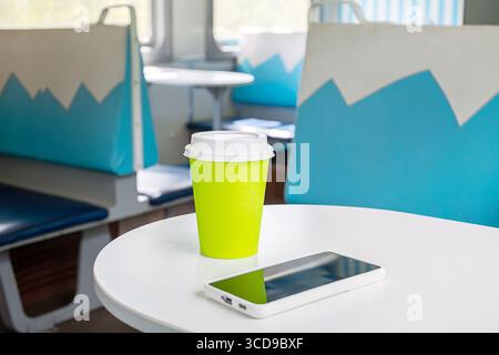 Tazza di caffè verde e smartphone su un tavolo in un vagone ferroviario. Viaggio, tour e viaggio da soli. Concetto di viaggio in solitaria confortevole. Foto Stock