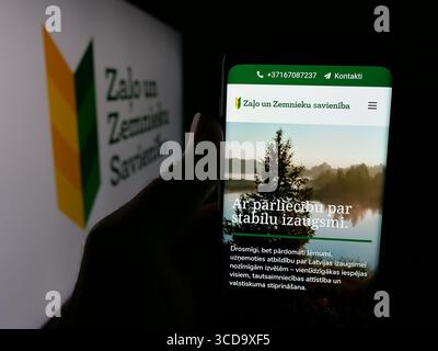 In questa illustrazione fotografica, una persona ha in mano uno smartphone con la pagina web del party Zalo un Zemnieku Savieniba (ZZS) sullo schermo davanti al logo. Foto Stock