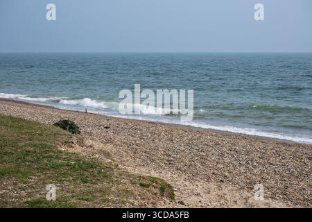 Spiaggia di ciottoli e ciottoli con dolci onde sotto un cielo limpido a Minsmere, sulla costa del Suffolk, in Inghilterra, affacciata sul Mare del Nord. Foto Stock