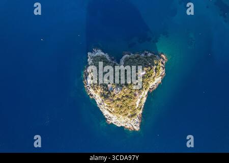 Vista aerea dell'isola a forma di cuore, un gioiello verdeggiante circondato dal mare blu profondo, testimonianza dell'arte della natura, l'isola di Bergeggi, la Liguria, l'Italia. Foto Stock