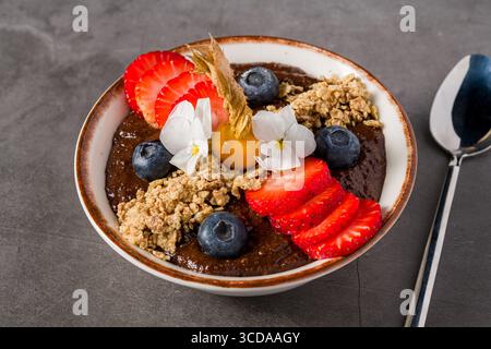 Ciotola per frullati di cioccolato tropicale con muesli, frutti di bosco e fiori commestibili Foto Stock