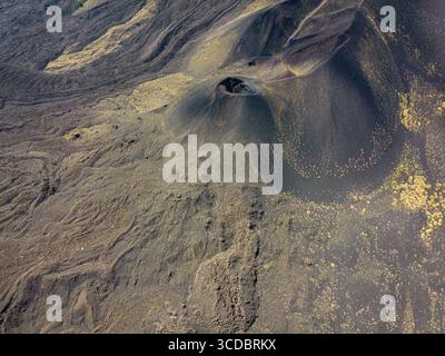 La vista aerea della cenere vulcanica scura e del terreno roccioso creano un paesaggio aspro e lunare, punteggiato dal cono di un piccolo cratere, Catania, Sicilia, Italia. Foto Stock