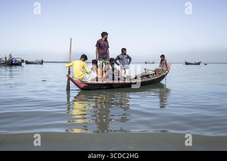 Cox's Bazar, Bangladesh - 29 novembre 2022: Veduta dei ragazzi locali raggruppati su una tradizionale barca di legno, la sua riflessione risplende sulle acque tranquille, sotto un cielo limpido ed esteso. Foto Stock