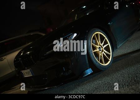 Calaone, italia 13 agosto 2025: Moderna bmw nera serie 5 parcheggiata di notte, con cerchi in lega dorata e luci anteriori Foto Stock