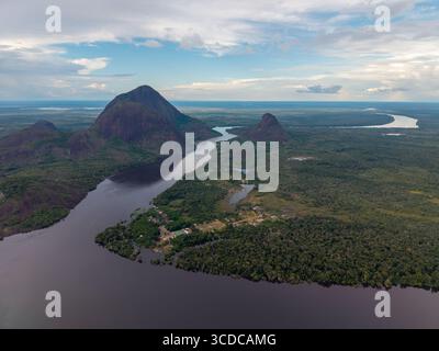 Vista aerea del fiume scuro che serpeggia attraverso la vibrante foresta pluviale verde, oscurato dall'imponente Cerros de Mavicure sotto un vasto cielo nuvoloso, Puerto Inírida, Cerros Mavicure, Colombia. Foto Stock