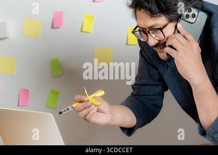 Un giovane uomo d'affari scrive idee su appunti e le attacca a un muro nel suo ufficio. Foto Stock