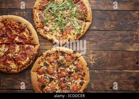 Composizione di tre tipi diversi di pizze poste su un tavolo di legno arrugginito e graffiato. Piatti caldi e freschi pronti da mangiare Foto Stock