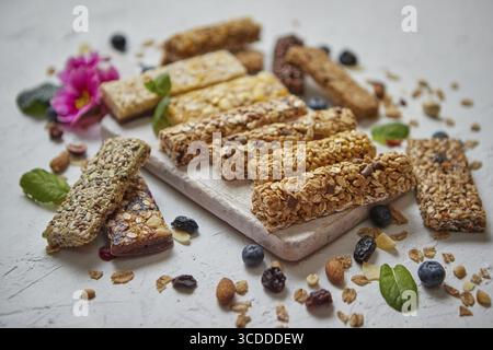Vari tipi di barrette di granola proteiche con frutta secca e frutti di bosco. Posizionato su un tagliere di legno bianco. Disposizione piatta, vista dall'alto Foto Stock