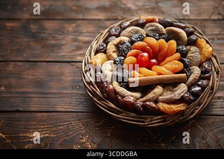 Mescolare la frutta secca in un piccolo cestello di vimini su un tavolo di legno. Assortimento di contais albicocche, prugne, fichi, datteri, ciliegie, pesche. Sopra la vista con copia Foto Stock