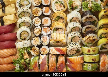 Vista dall'alto sullo sfondo con set di diversi tipi colorati di panini di sushi posti su tavola di legno. Disposizione piatta Foto Stock