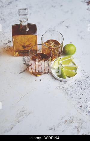 Bevanda acida di whisky con calce in vetro su fondo rustico in pietra. Due bicchieri riempiti di ghiaccio e caraffa Foto Stock