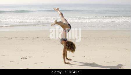 Giovane donna afroamericana che fa il cartwheel sulla spiaggia al rallentatore Foto Stock