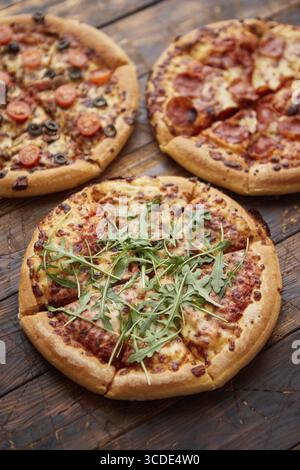 Composizione di tre tipi diversi di pizze poste su un tavolo di legno arrugginito e graffiato. Piatti caldi e freschi pronti da mangiare Foto Stock