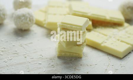 Barra di cioccolato bianco con piccoli pezzi collocati in prossimità di uno su un altro e dolci rotonda ricoperta con scaglie di noce di cocco sulla tovaglia bianca Foto Stock