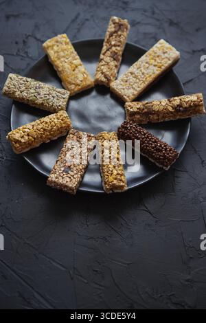 Diversi tipi di barrette in granola poste su un piatto di ceramica nera su un tavolo. Concetto di dieta sana. Vista superiore con spazio di copia Foto Stock