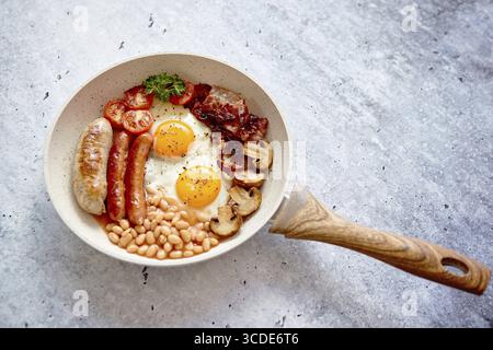 Colazione inglese completa con salsicce, pomodori alla griglia, funghi, uova, pancetta fagioli e pane al forno. Vista dall'alto Foto Stock