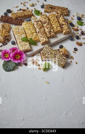 Vari tipi di barrette di granola proteiche con frutta secca e frutti di bosco. Posizionato su un tagliere di legno bianco. Disposizione piatta con spazio di copia Foto Stock