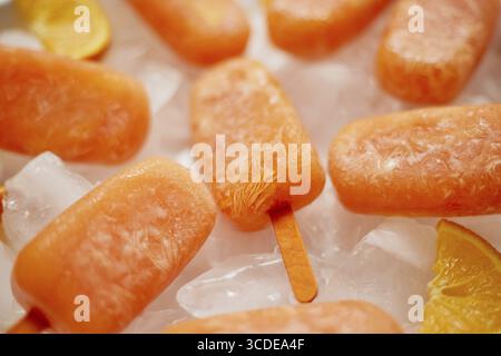 Papaveri surgelati fatti in casa realizzati con arance fresche oragniche posizionate con cubetti di ghiaccio sul tavolo di marmo. Disposizione piatta, vista dall'alto Foto Stock