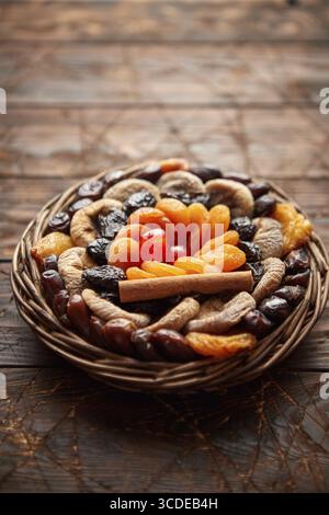 Mescolare la frutta secca in un piccolo cestello di vimini su un tavolo di legno. Assortimento di contais albicocche, prugne, fichi, datteri, ciliegie, pesche. Sopra la vista con copia Foto Stock