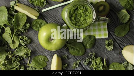 Da sopra il colpo di composizione di verde con un fresco e mela matura e fette di kiwi sul tavolo di legno con i frullati in vaso e verdure fresche Foto Stock
