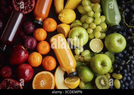 Vari frutti e verdure sani formati in composizione arcobaleno. Posto su un tavolo di legno nero. Con i biberon sul succo appena spremuto Foto Stock
