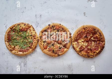 Tre tipi diversi di pizze. Posto in fila su un tavolo bianco arrugginito. Visualizza dall'alto con uno spazio per il testo Foto Stock