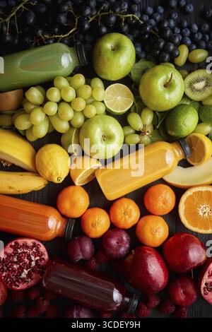 Vari frutti e verdure sani formati in composizione arcobaleno. Posto su un tavolo di legno nero. Con i biberon sul succo appena spremuto Foto Stock
