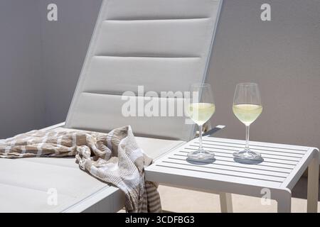 Rilassanti lettini con asciugamani ben piegati e due bicchieri di vino bianco freddo su un tavolino. Foto Stock