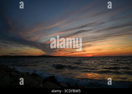 Tramonto colorato che illumina una costa rocciosa mentre le dolci onde si infrangono contro la riva. Foto Stock