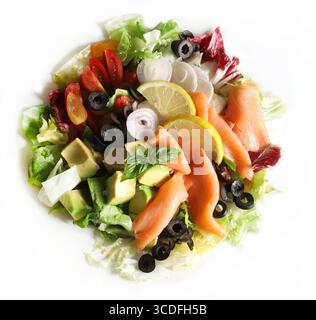 Insalata con salmone affumicato, avocado, olive, limone, lattuga e verdure fresche su un piatto bianco. Cibo sano. Direttamente sopra. Foto Stock
