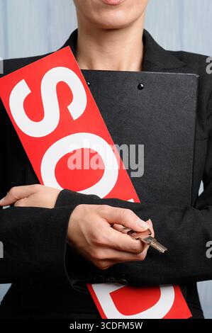 Agente immobiliare che tiene in mano la chiave di un immobile mentre stringe un cartello di vendita, primo piano Foto Stock