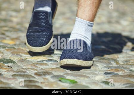 Primo piano delle gambe dell'uomo che camminano lungo il vicolo acciottolato. Concetti di esplorare strade nascoste, momenti di viaggio spontanei, viaggi nelle vecchie città d'Europa Foto Stock