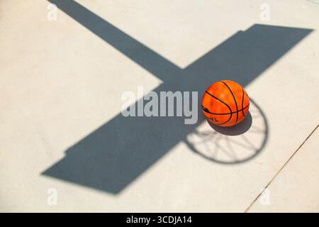 Una pallacanestro per terra di un campo all'ombra del tabellone Foto Stock
