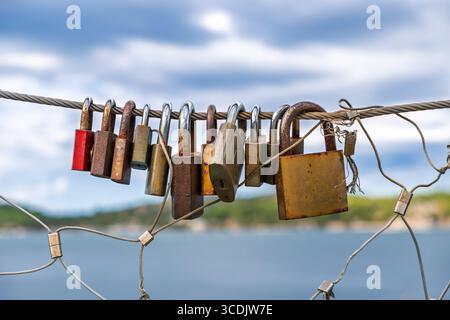 Una fila di vecchi e arrugginiti d'amore si chiude su un cavo d'acciaio, simboleggiando l'amore e l'impegno eterni. I lucchetti d'amore, simbolo della tradizione romantica, sono appesi al ponte Foto Stock