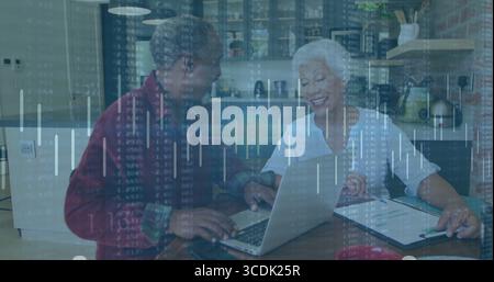 Coppia senior che esamina i dati finanziari su un notebook argentato in una cucina moderna, con appunti e penna Foto Stock