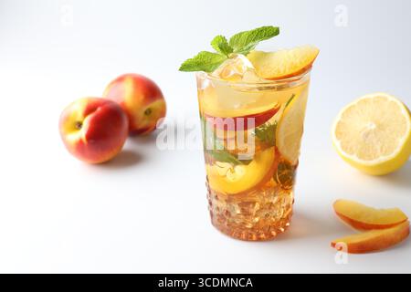 Gustoso tè freddo con limone, pesche e menta su sfondo bianco Foto Stock