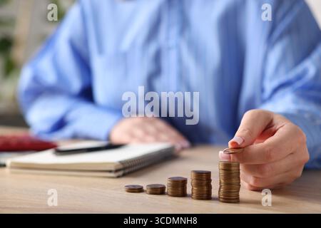 Donna impilando monete a tavola di legno, primo piano Foto Stock