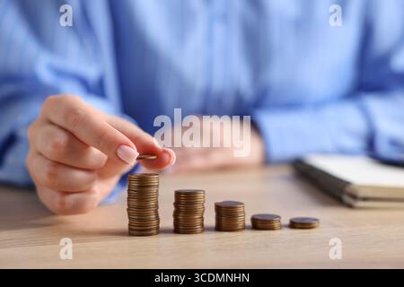Donna impilando monete a tavola di legno, primo piano Foto Stock