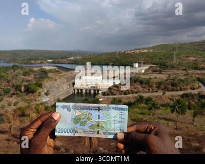 (250813) -- DUBREKA (GUINEA), 13 agosto 2025 (Xinhua) -- foto scattata il 3 maggio 2025 mostra una banconota da 000 franchi della Guinea recante l'immagine della centrale idroelettrica di Kaleta con la centrale idroelettrica di Kaleta sullo sfondo a Dubreka, Guinea. Sul fiume Konkoure che scorre giù dagli altopiani di Fouta Djallon nella Guinea centrale, l'impressionante struttura della centrale idroelettrica di Kaleta si riflette nelle acque. La struttura ha fornito elettricità stabile alla capitale nazionale di Conakry e ai villaggi delle montagne settentrionali, ora presenti sulla banconota da 000 franchi della Guinea, che mostra un st Foto Stock