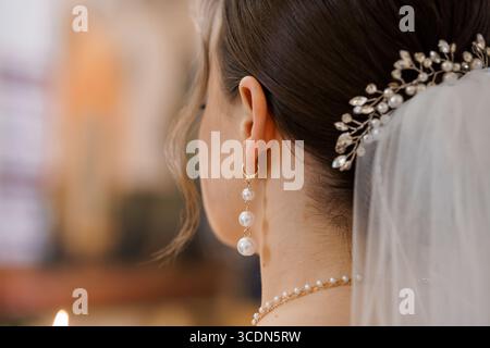 Incredibile foto ravvicinata di una sposa che indossa un delicato pettine per capelli perlati e orecchini con un velo che scorre, gioielli dorati, che catturano romantiche nozze Foto Stock