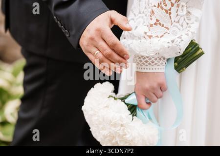 Primo piano di uno sposo che mette una fede nuziale sul dito della sposa durante una cerimonia, tenendo un bouquet bianco, simboleggia l'amore e l'impegno, eleg Foto Stock
