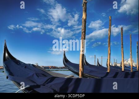 Venezia, Italia. Primo piano di gondole legate a palafitte contro un cielo blu brillante. Foto Stock