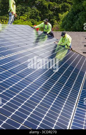 Uomini che indossano imbracature di sicurezza sul tetto che installano LG NeonR Pannelli fotovoltaici CC su guide in alluminio durante un fotovoltaico residenziale installare Foto Stock