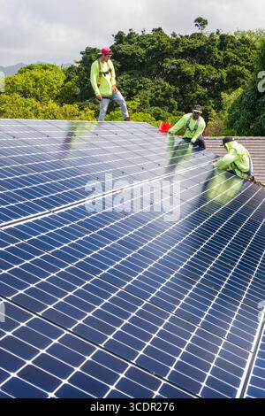 Uomini che indossano imbracature di sicurezza sul tetto che installano LG NeonR Pannelli fotovoltaici CC su guide in alluminio durante un fotovoltaico residenziale installare Foto Stock