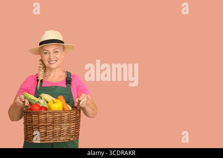 Agricoltore maturo con cesto di vimini pieno di diverse verdure mature su sfondo arancione Foto Stock