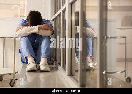 Infermiera maschile stressata seduta su davanzale in ospedale di sera Foto Stock