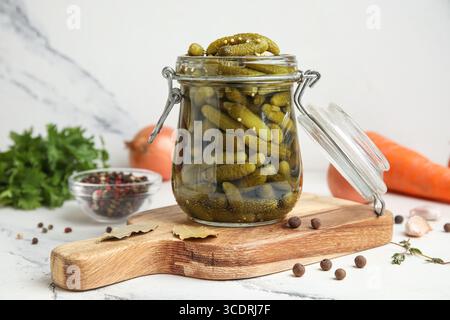 Barattolo con gustosi cetrioli sottaceto e spezie diverse su sfondo bianco Foto Stock