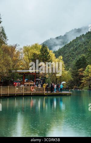 Lijiang, Cina - 24 ottobre 2024: I turisti si riuniscono su una piattaforma di osservazione in legno sulle acque turchesi, circondati da alberi colorati nella Blue Moon Valley, L. Foto Stock
