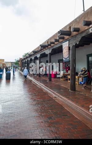 Persone che camminano su asfaltatrici bagnate di mattoni rossi di fronte al Palazzo dei governatori dopo una tempesta di pioggia monsonica, Santa Fe, New Mexico, Stati Uniti Foto Stock